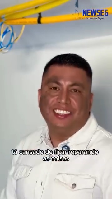 Consultor da Newseg ao lado de uma escada, sob um forro com fiação aparente, falando à câmera sobre seguro residencial